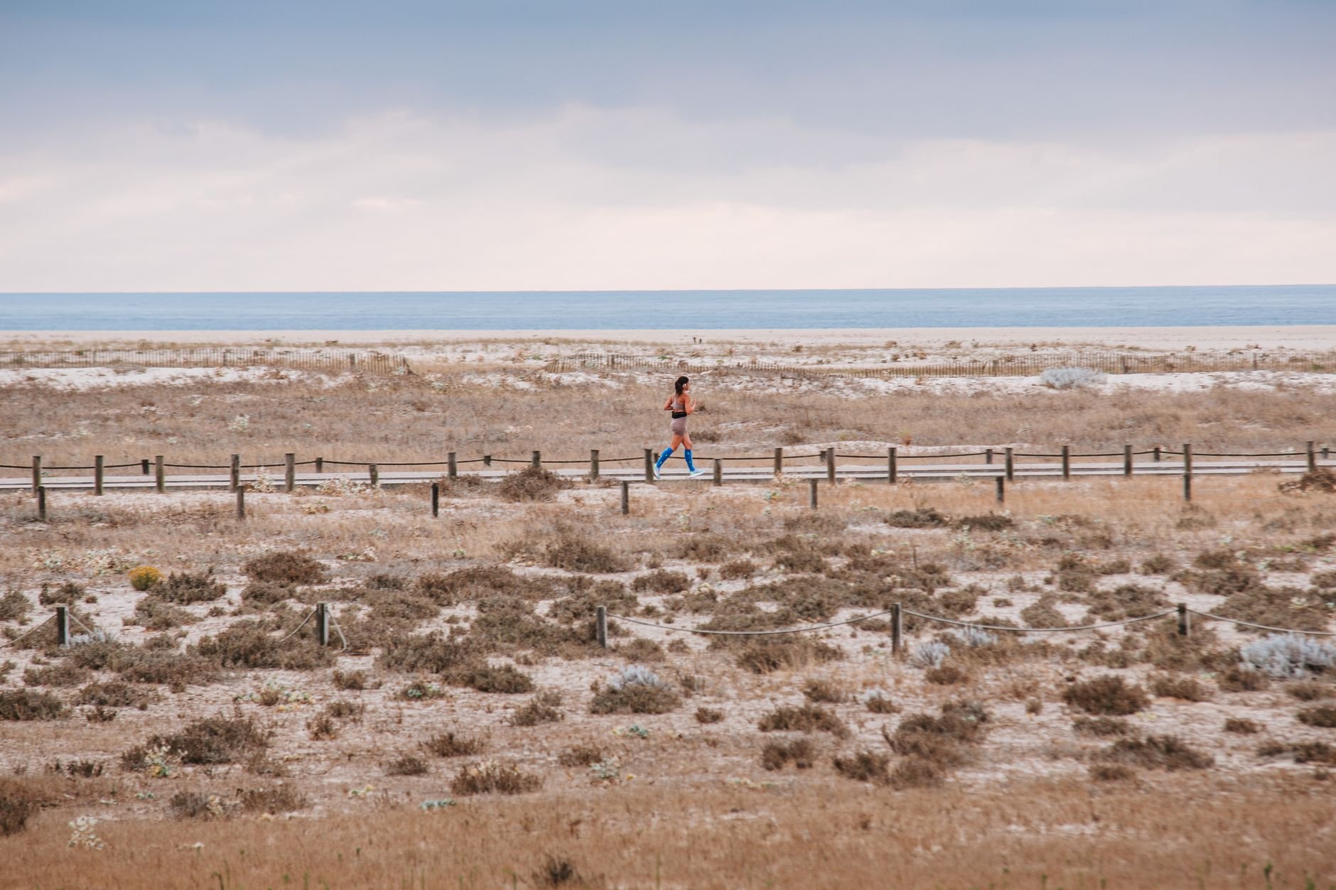 Runner on a sandy coastal path with ocean backdrop, early day exercise.